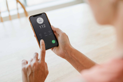 Cilvēkam rokā mobilais telefons, kas zvana uz numuru "112"