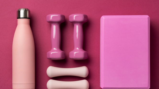 Veselīga dzīvesveida aprīkojums: ūdens pudele, hanteles uz roza fona