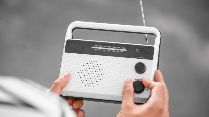 Balts radio aparāts, ko tura sievietes rokas