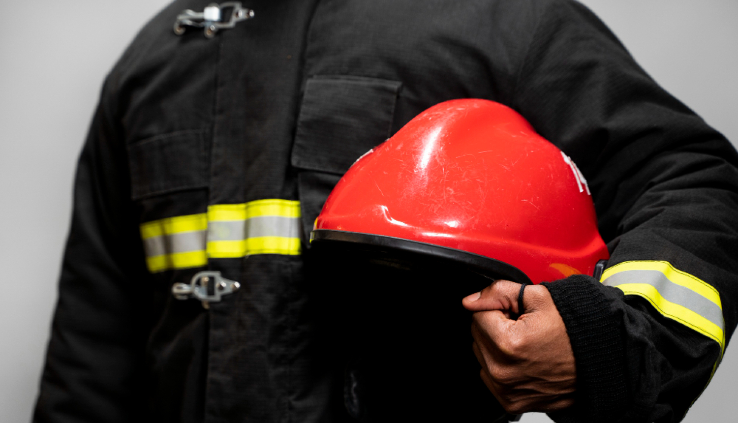 Ugunsdzēsējs tura rokās ķiveri, redzams tikai rumpis ar roku.