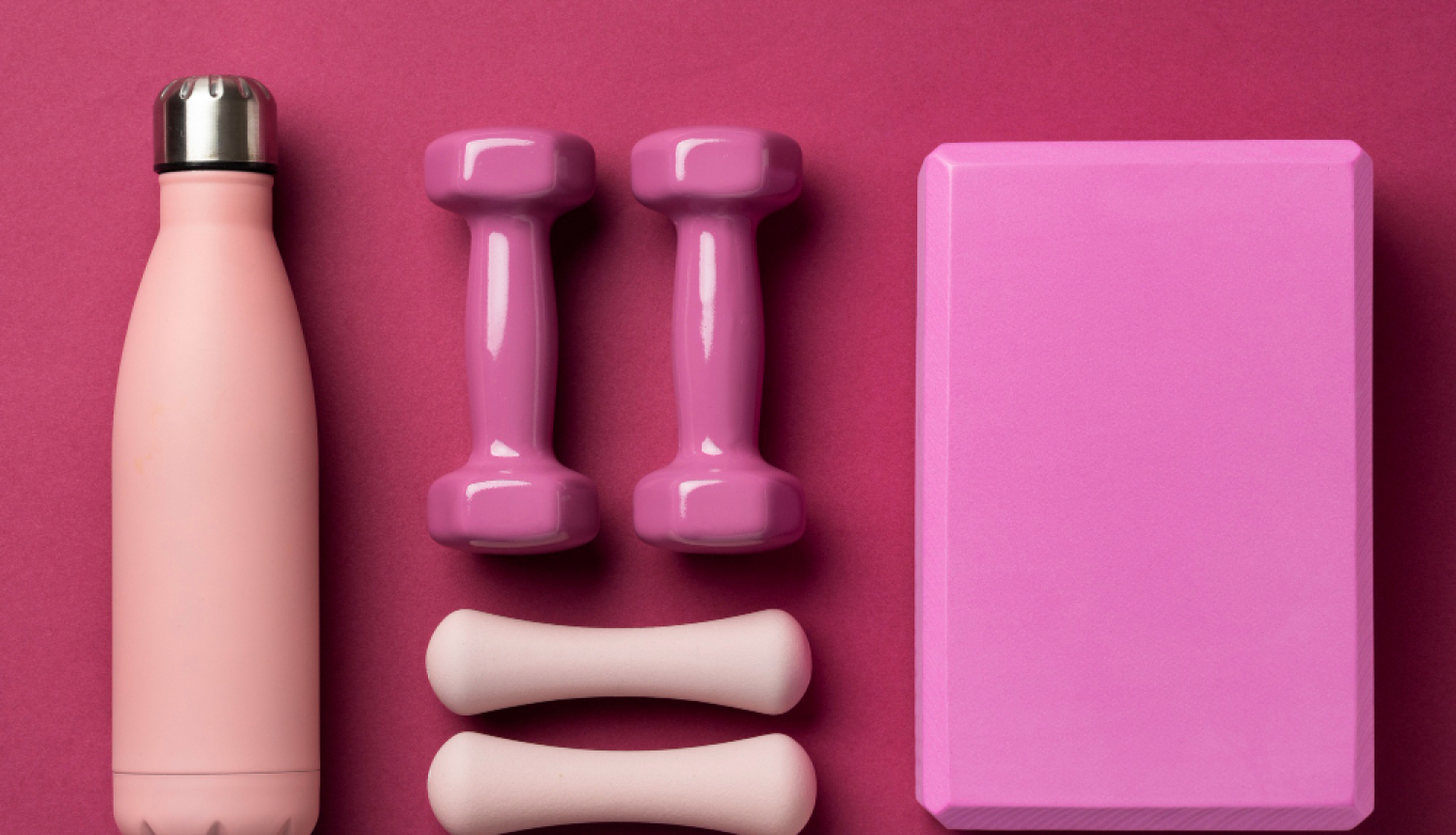 Veselīga dzīvesveida aprīkojums: ūdens pudele, hanteles uz roza fona